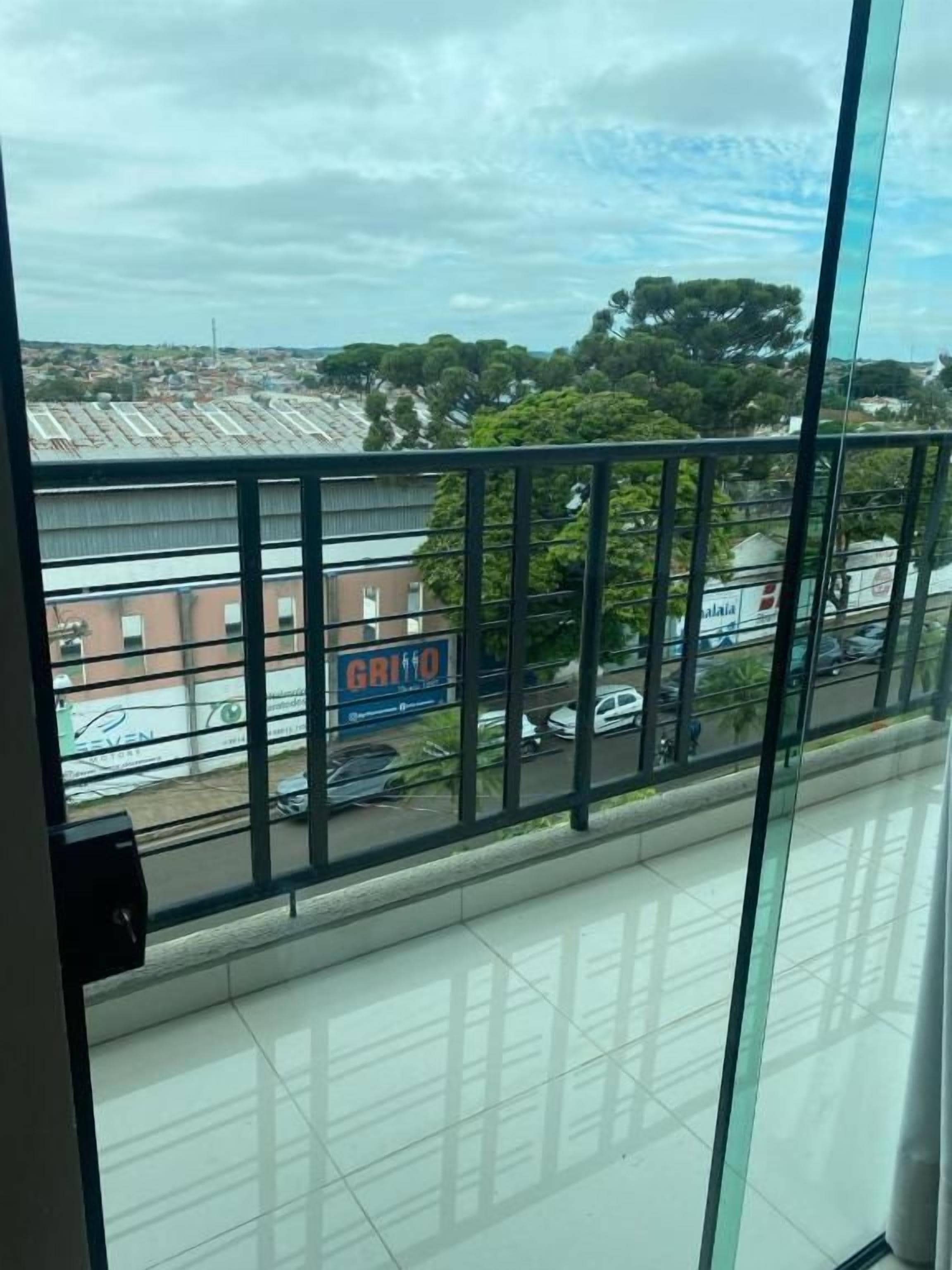 A view from a window with a metal railing, a clear sky, and a distant building with a sign.