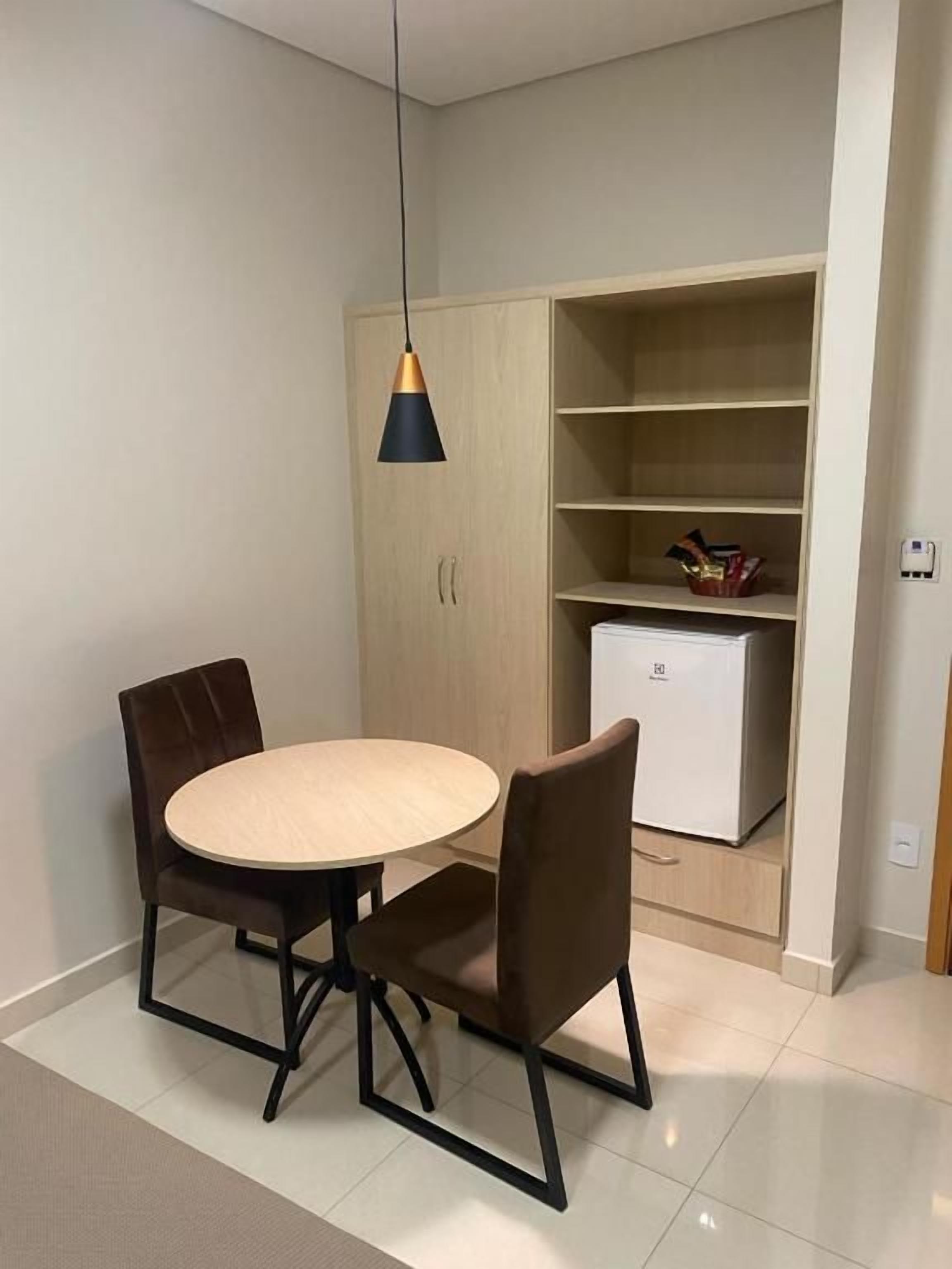 Un comedor con una mesa redonda y sillas, una lámpara colgante, un armario de madera empotrado y un electrodoméstico blanco.