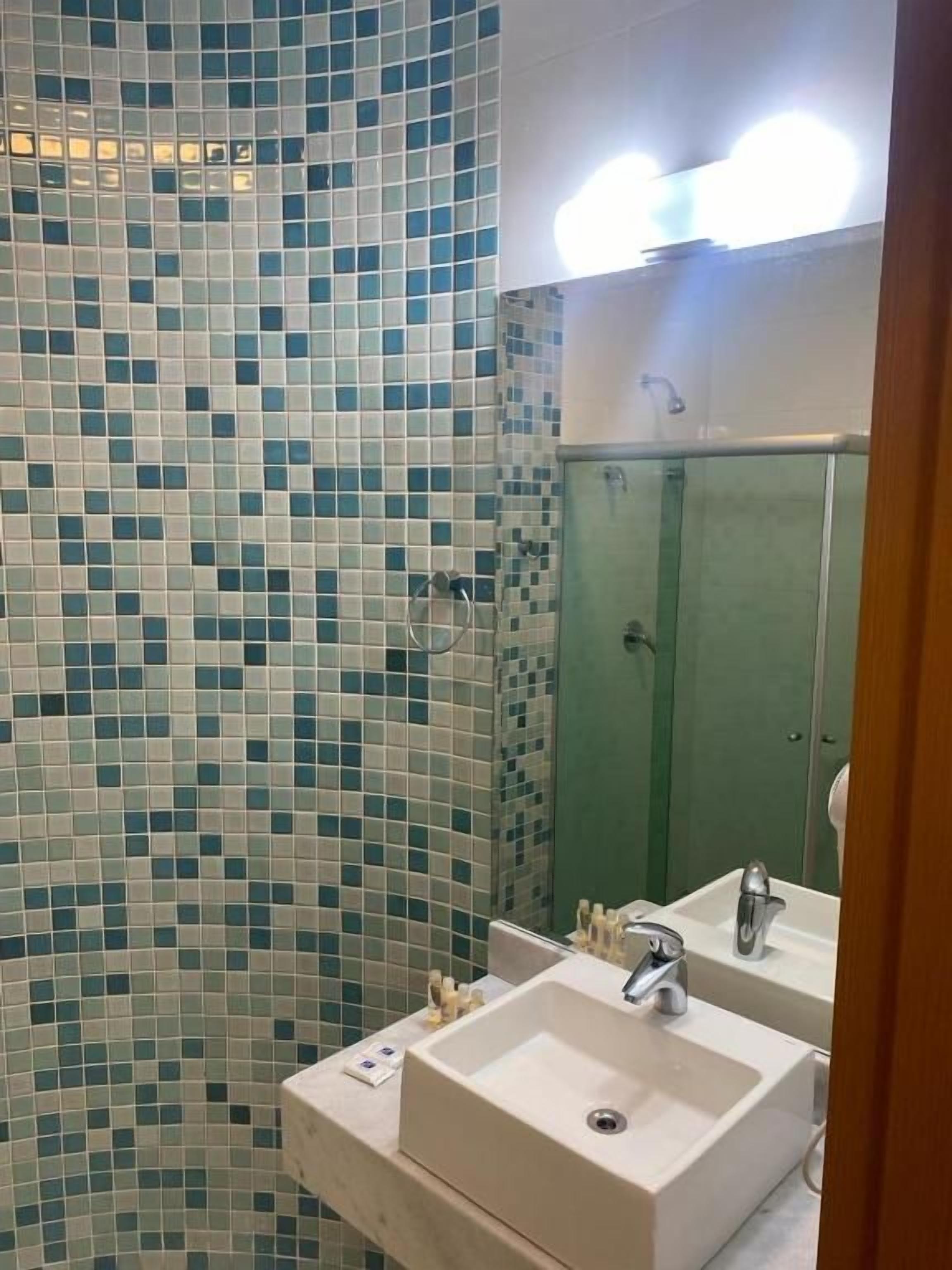 Un baño con pared de azulejos, lavamanos, espejo y zona de ducha.