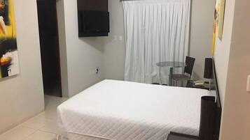 A hotel room with a bed, a small table with chairs, a TV mounted on the wall, and an air conditioning unit.