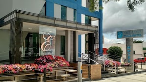 Het exterieur van het EXCELLENCE PLAZA HOTEL met een modern ontwerp, met een opvallend logo, een trap naar de ingang en een bord.
