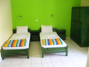 Una habitación con dos camas individuales, cabeceros verdes, ropa de cama blanca y un armario verde.