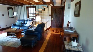 A cozy living room with a leather sofa, a coffee table, and a dining table with chairs. There is a wooden door and a window with blinds. - Beautiful, 200 year old Log home - Secluded, 30 Min. from Downtown (Indianapolis, Acton)