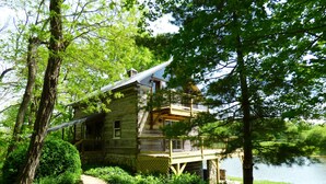 A rustic cabin with a balcony, surrounded by lush greenery and a lake. - Beautiful, 200 year old Log home - Secluded, 30 Min. from Downtown (Indianapolis, Acton)