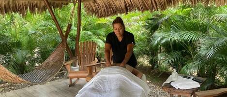 A massage area with a thatched roof, wooden chairs, and a massage table covered with a white sheet.