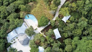 An aerial view of a resort with multiple tree-covered areas, a swimming pool, and several white-roofed structures. - Mikado Natural Lodge (Tamarindo)