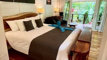 Ein Hotelzimmer mit einem großen Bett, einem Holzkopfende, einem Balkon mit Blick auf Grünflächen und einem Gemälde an der Wand.