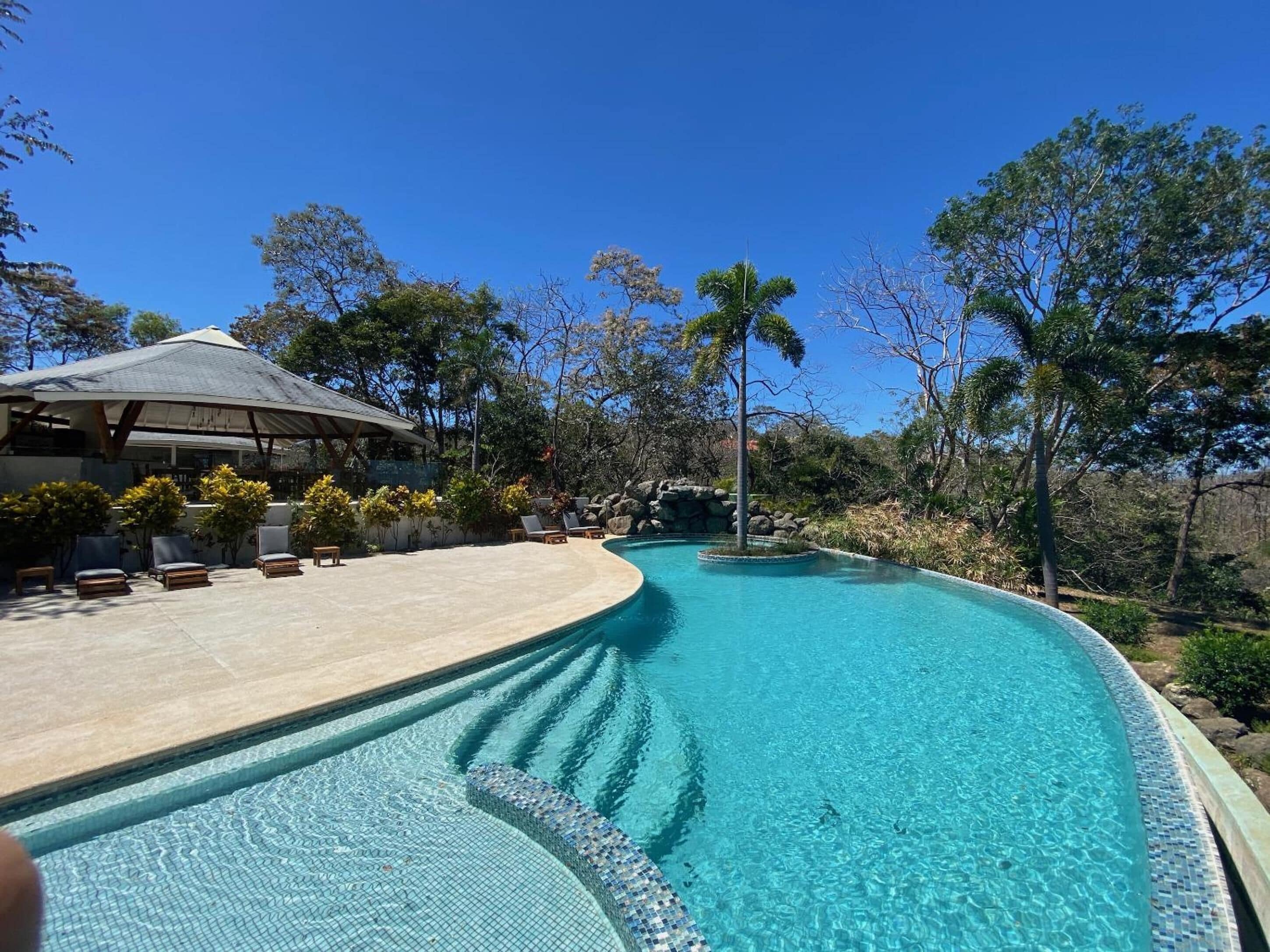 Una piscina al aire libre, sombrillas, sillones reclinables de piscina
