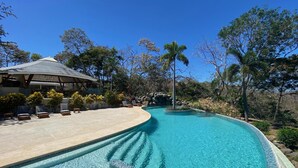 A swimming pool with a tiled edge, surrounded by lounge chairs and a covered seating area. - Mikado Natural Lodge (Tamarindo)
