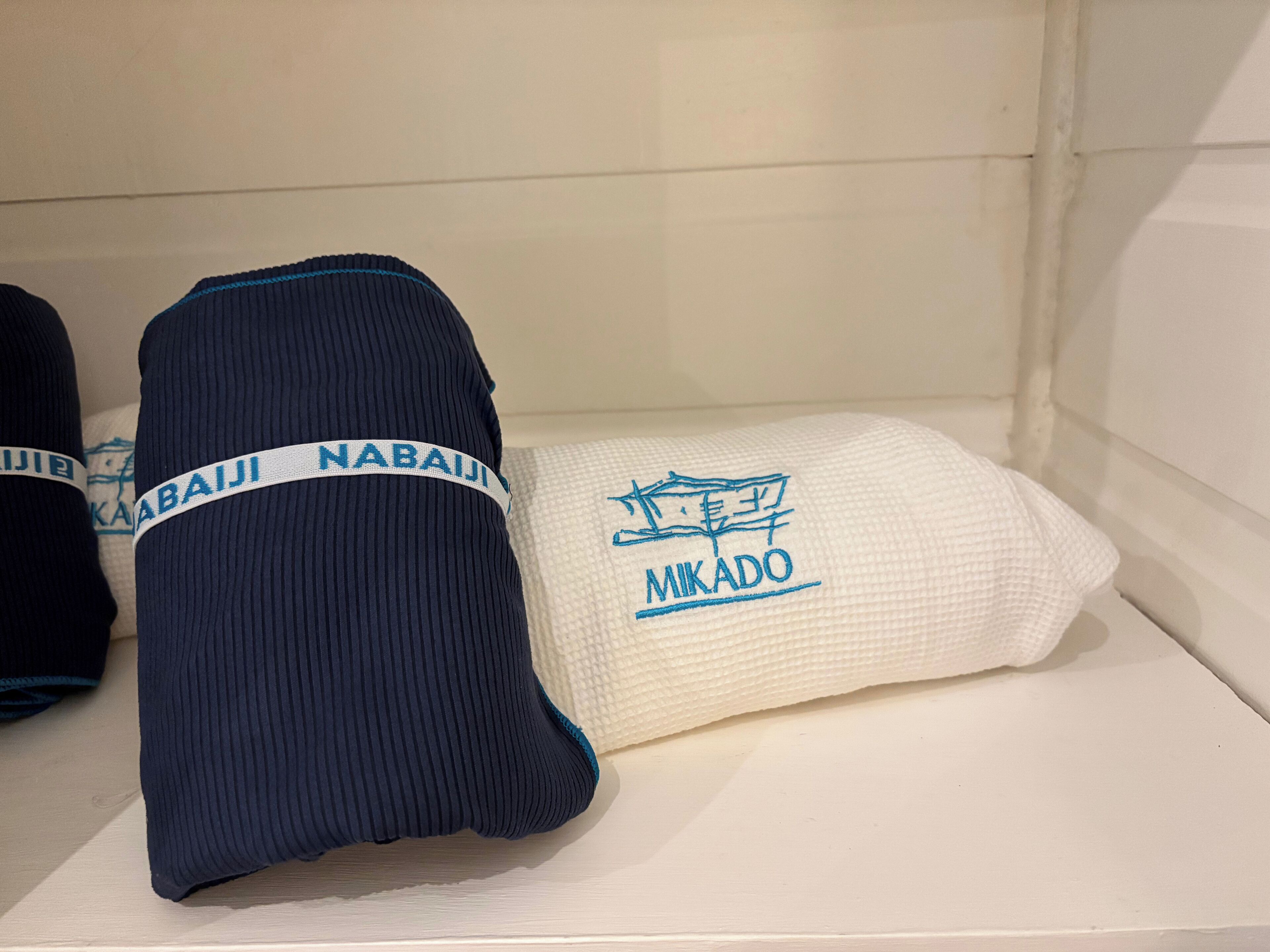En hylla med två ihopvikta föremål, ett mörkblått och ett vitt, med broderad text.