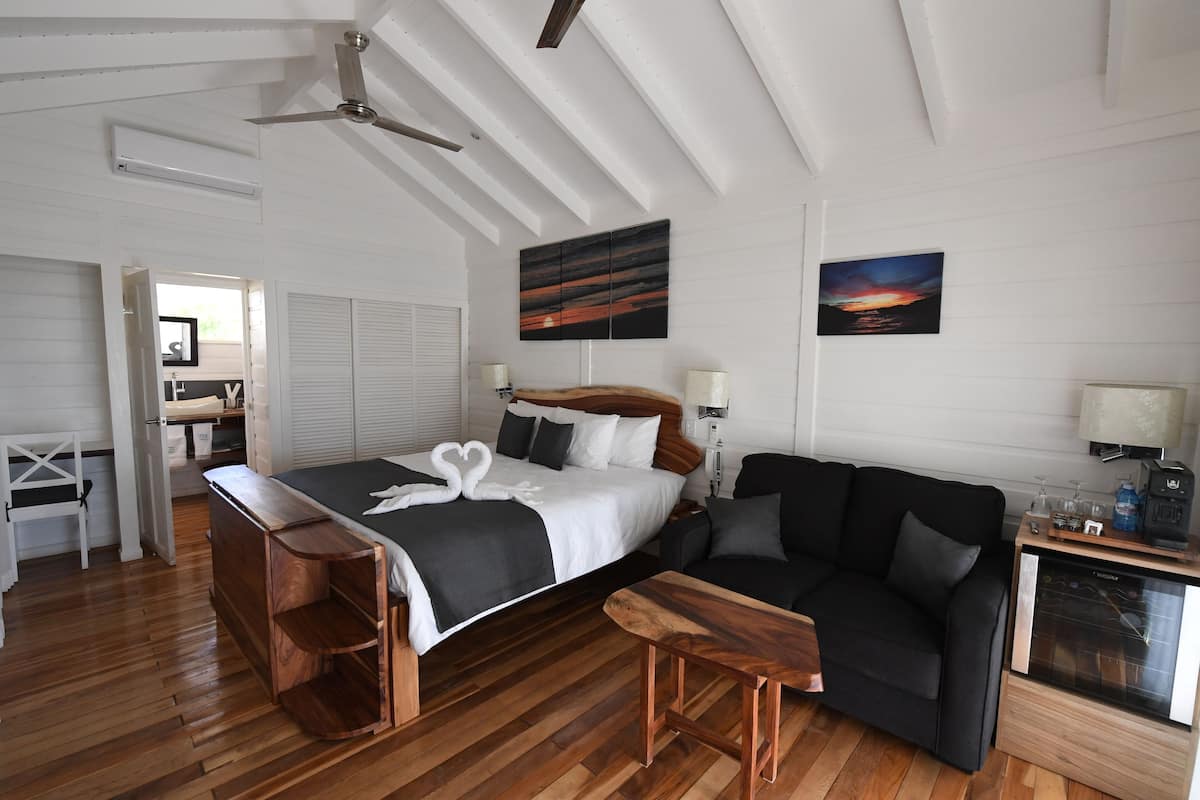 A bedroom with a bed, a wooden bench, a black sofa, a TV, and a ceiling fan.