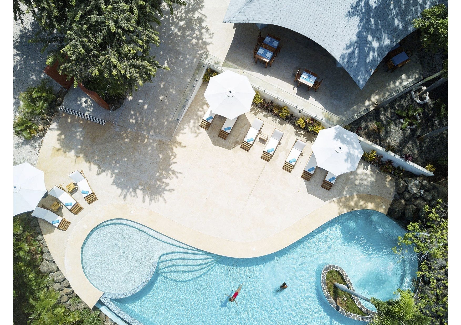 An aerial view of a resort with a swimming pool, lounge chairs, and umbrellas.