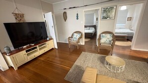 A living room with a TV, wicker chairs, a round coffee table, and a hallway leading to a bedroom. - Marlene Court -  Air con, boat parking (South West Rocks)