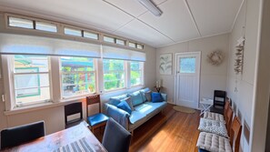 A room with a large window, a sofa, a dining table, and a door. - Marlene Court -  Air con, boat parking (South West Rocks)