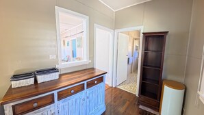 A hallway with a wooden cabinet, a tall dark bookshelf, and a window with a view into another room. - Marlene Court -  Air con, boat parking (South West Rocks)