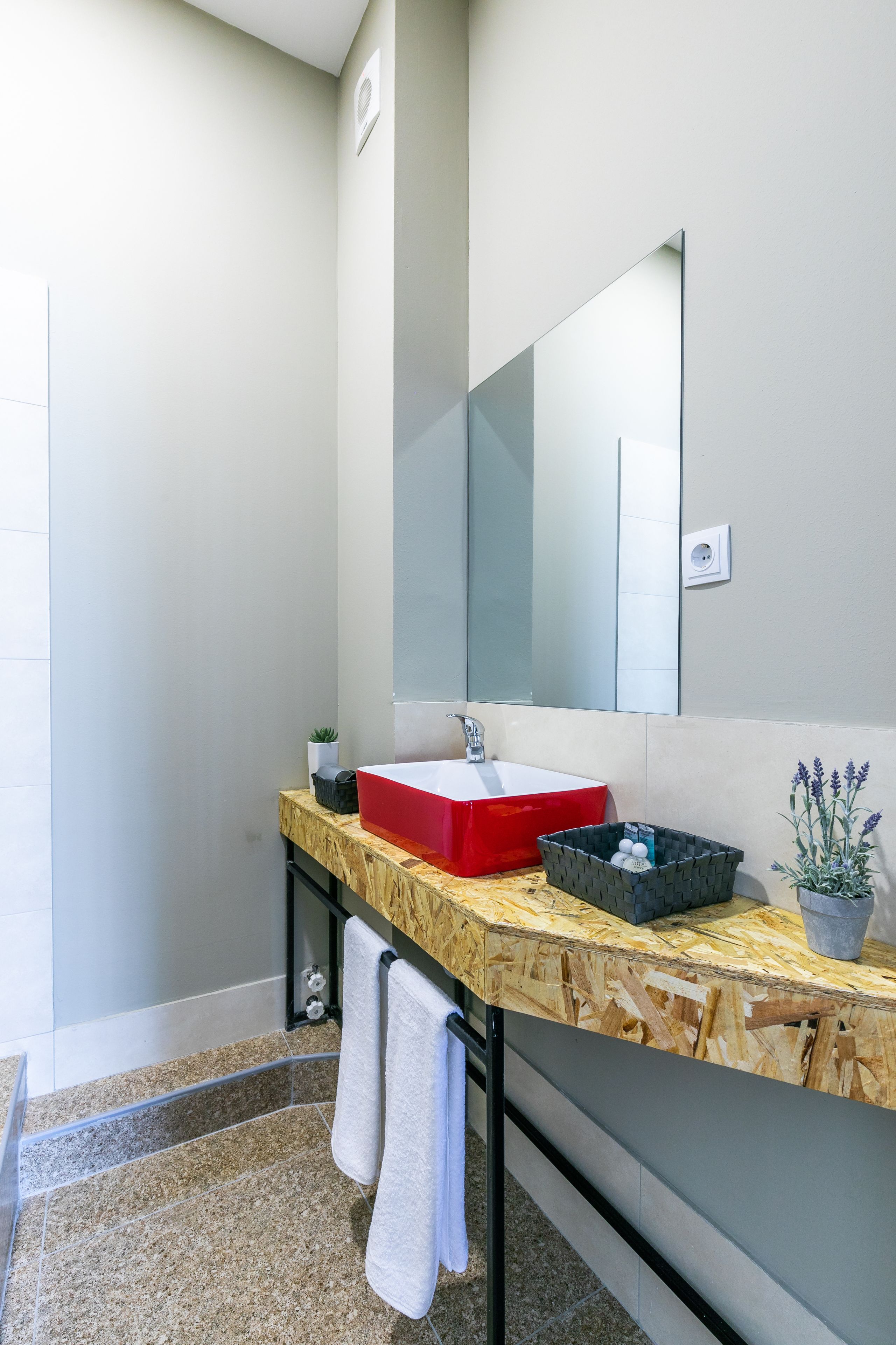 A modern bathroom with a wooden vanity, a red sink, and a large mirror.