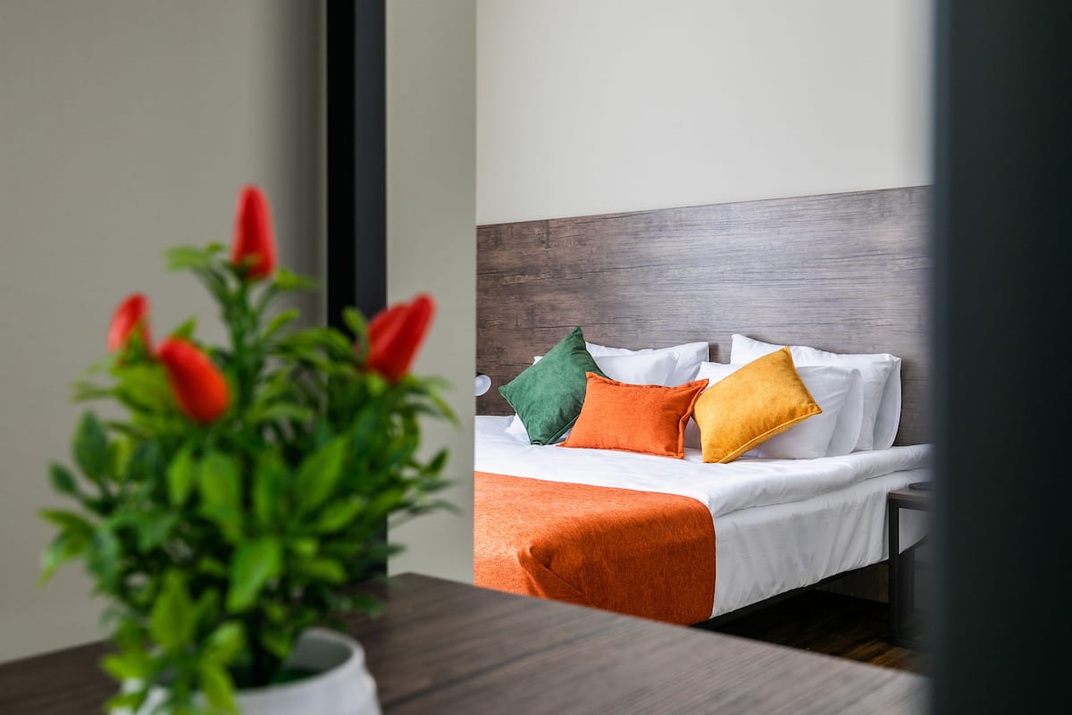 A hotel room with a bed, pillows, a bedside table, and a potted plant.