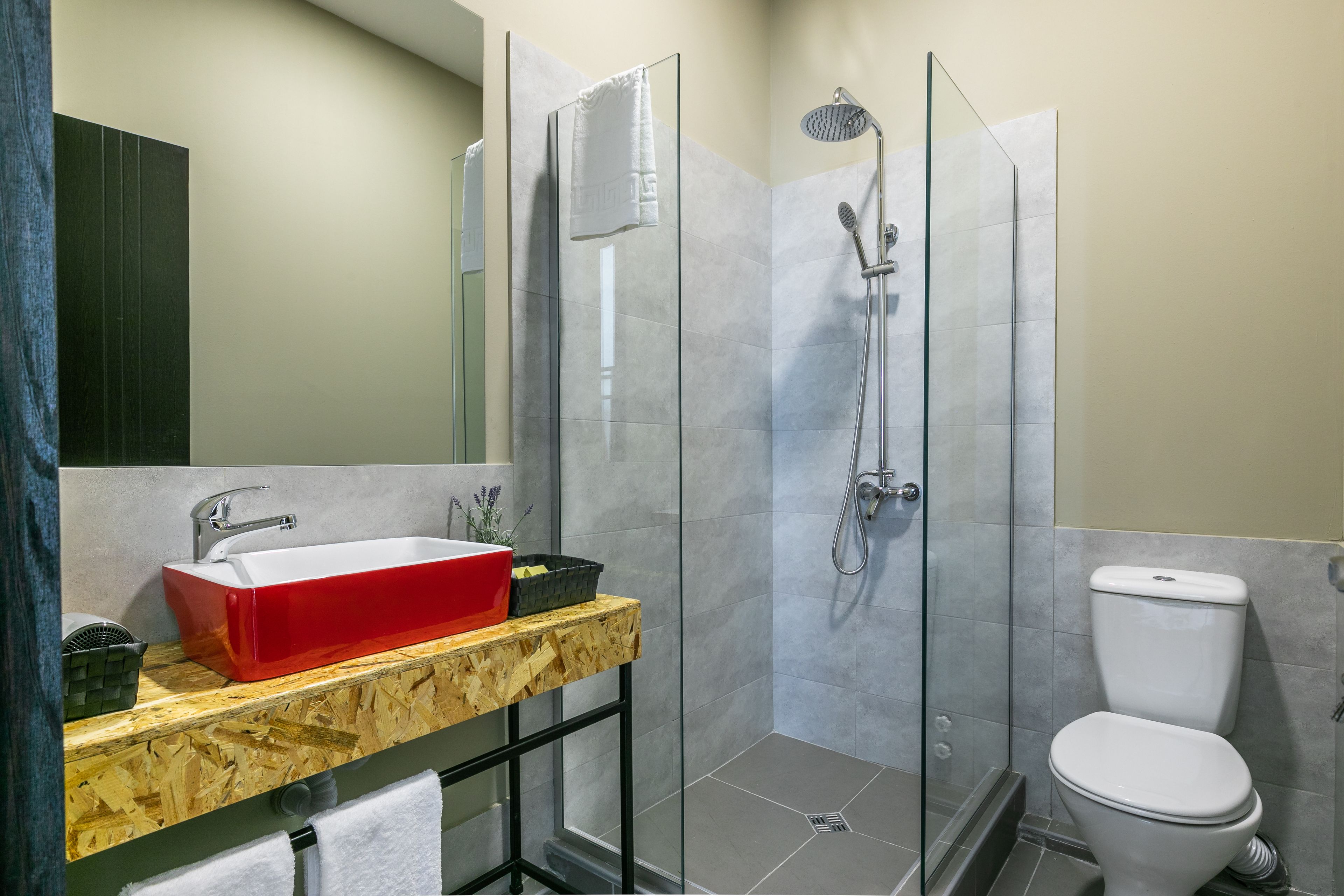 A modern bathroom with a glass shower enclosure, a red basin, and a toilet.