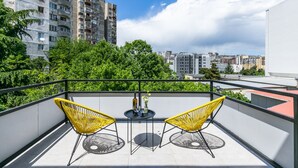 A balcony with two yellow chairs, a small table with a bottle and flowers, and a cityscape view. - Boutique Hotel MOJO (Tbilisi)