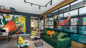 A modern interior with a green sofa, colorful artwork, and a bright window. - Boutique Hotel MOJO (Tbilisi)
