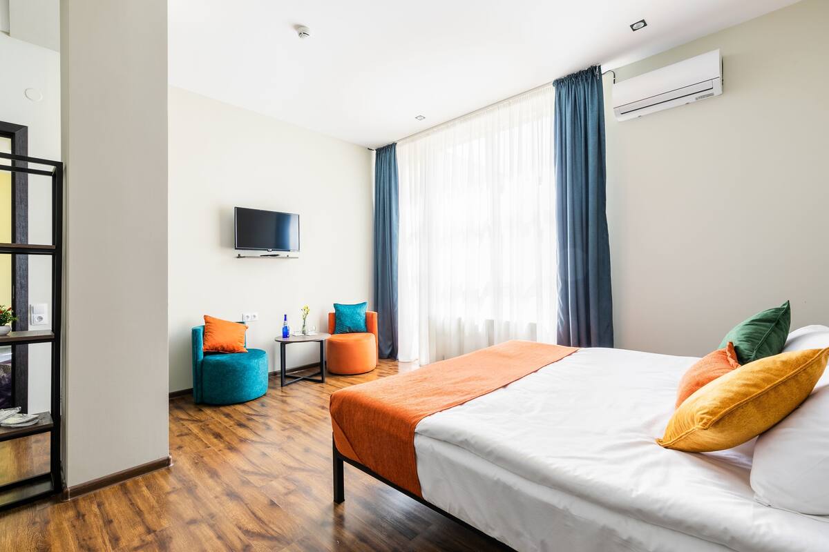 A hotel room with a bed, a TV, a desk, a chair, and a window with curtains.