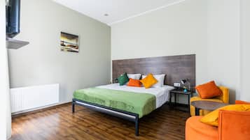 Un dormitorio moderno con suelo de madera, una cama con ropa de cama verde y naranja, una mesita de noche, una silla y una fotografía de un puente en la pared.