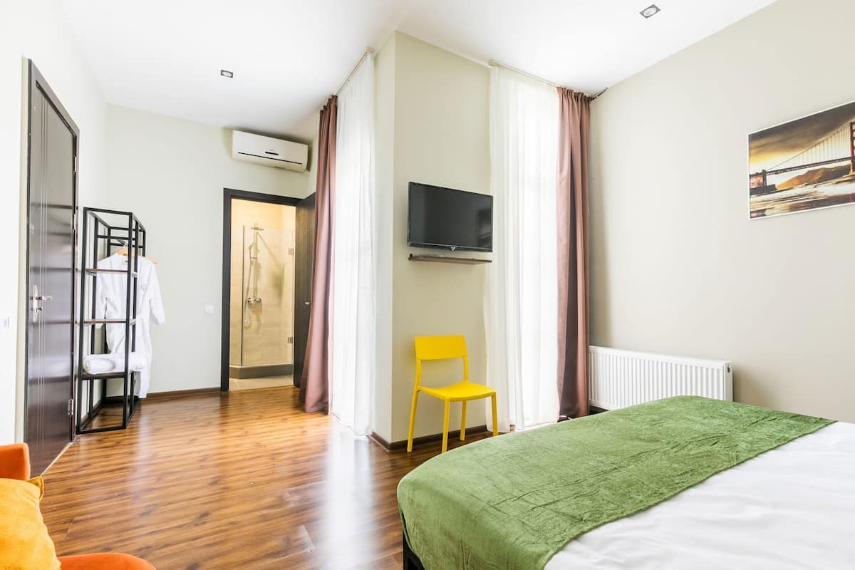 A hotel room with a bed, a TV, a shower, and a yellow chair.