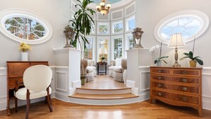 Une pièce spacieuse avec un plancher en bois, une chaise blanche, une commode en bois et une grande fenêtre donnant sur des arbres.