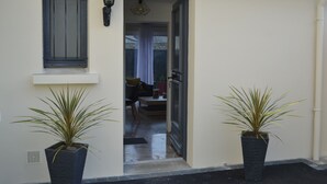 Uma porta de entrada dá acesso a uma sala de jantar com mesa e cadeiras, com dois vasos de plantas de cada lado.