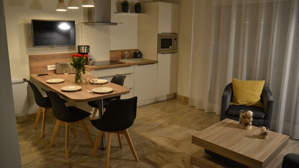Uma cozinha moderna com uma mesa de jantar, cadeiras e uma máquina de café. Há uma TV fixada na parede e um micro-ondas na bancada.