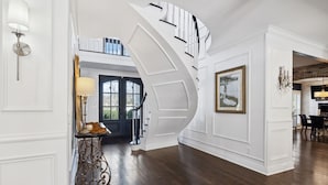 Eine prächtige Treppe führt zu einer zweiten Etage, eine Chandelüster und ein gerahmtes Bild an der Wand.