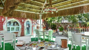 Un área de comedor al aire libre con mobiliario de mimbre blanco, techo de paja y piso de césped artificial verde.