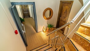 Una escalera de mármol con barandilla, una puerta de madera con espejo y suelo alfombrado.