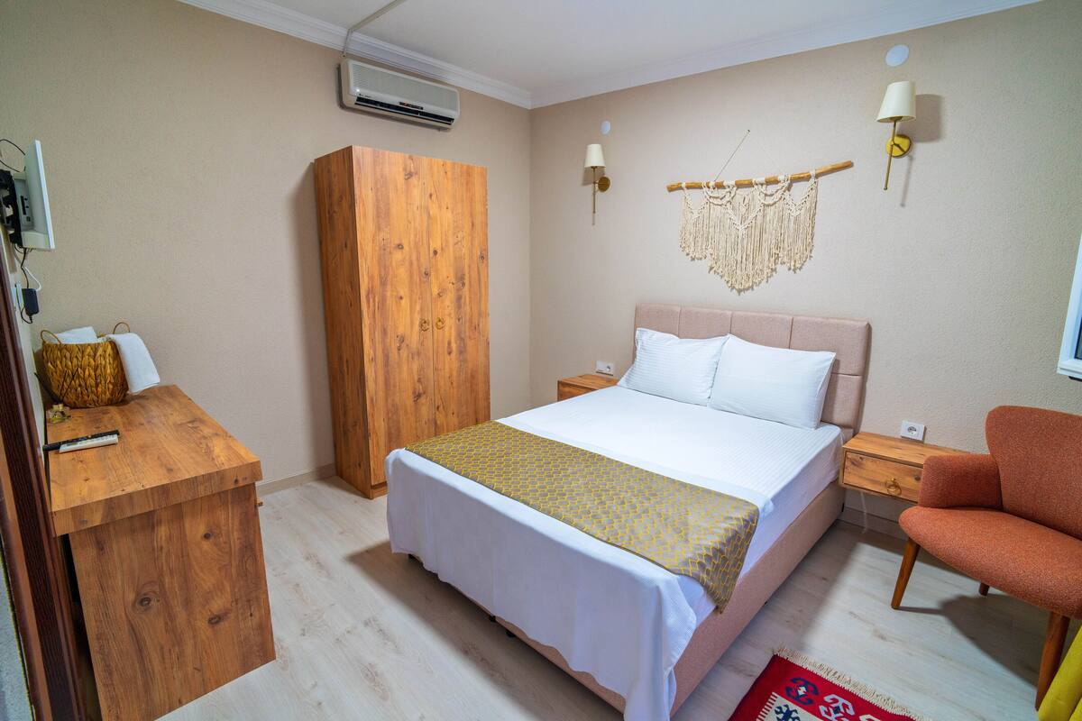 A bedroom with a bed, wooden wardrobe, bedside table, lamp, and a chair.