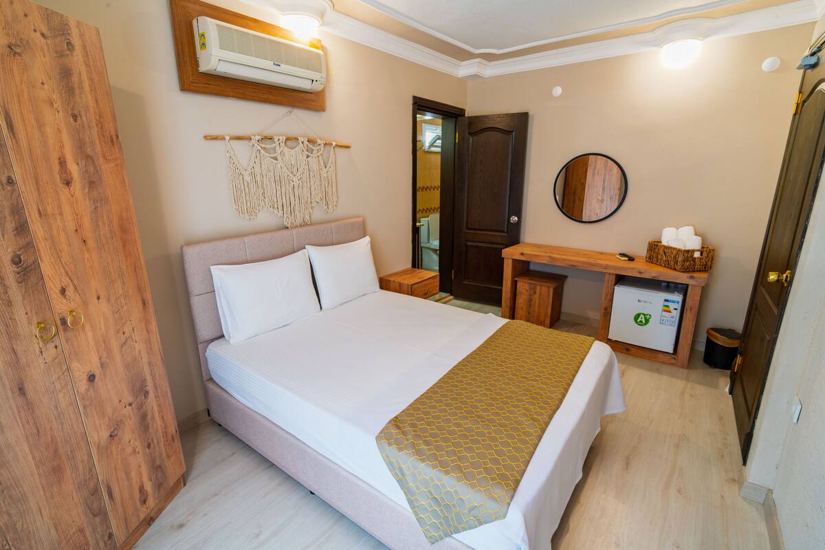 A bedroom with a bed, wooden wardrobe, bedside table, and a small desk with a basket.
