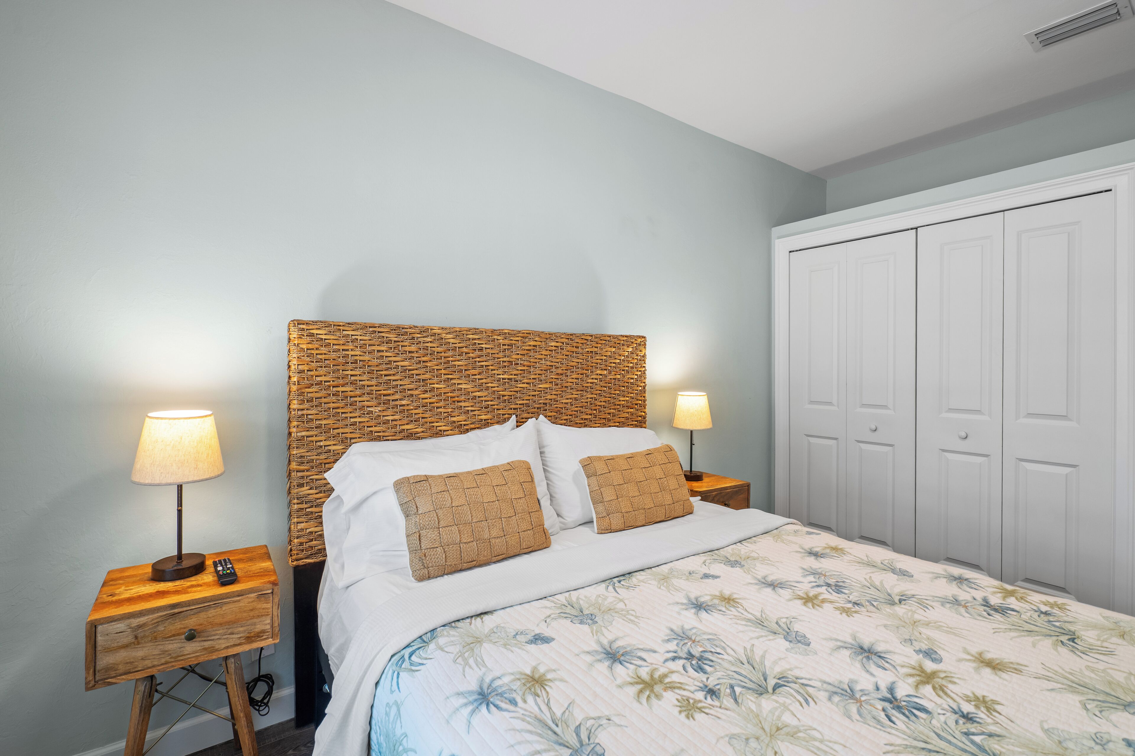 A bedroom with a wooden headboard, white bedding, two bedside lamps, a nightstand with a drawer, and a wardrobe.