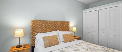 A bedroom with a wooden headboard, white bedding, two bedside lamps, a nightstand with a drawer, and a wardrobe.