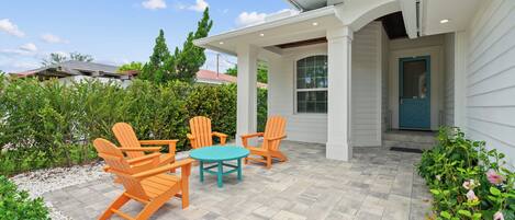 An outdoor patio with a table and four chairs, surrounded by greenery and a stone pathway.
