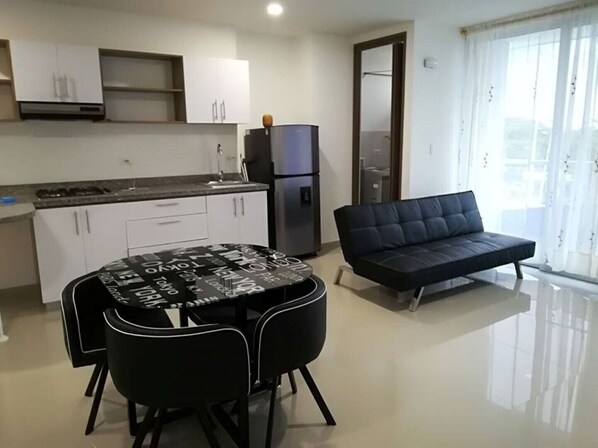 A modern kitchen with white cabinets, a black dining table with chairs, and a black sofa.