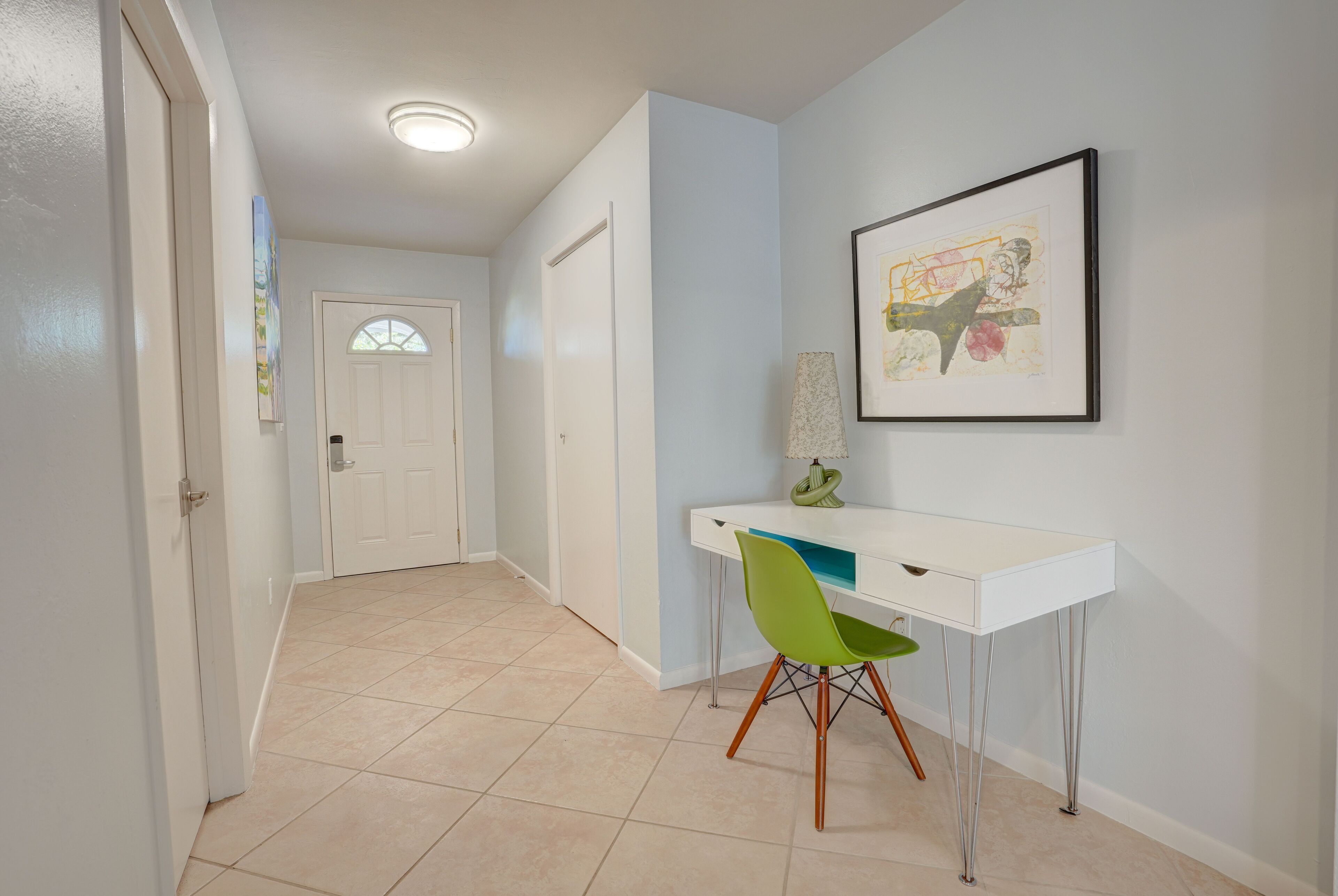 A hallway with a white desk, a green chair, and a framed artwork on the wall.