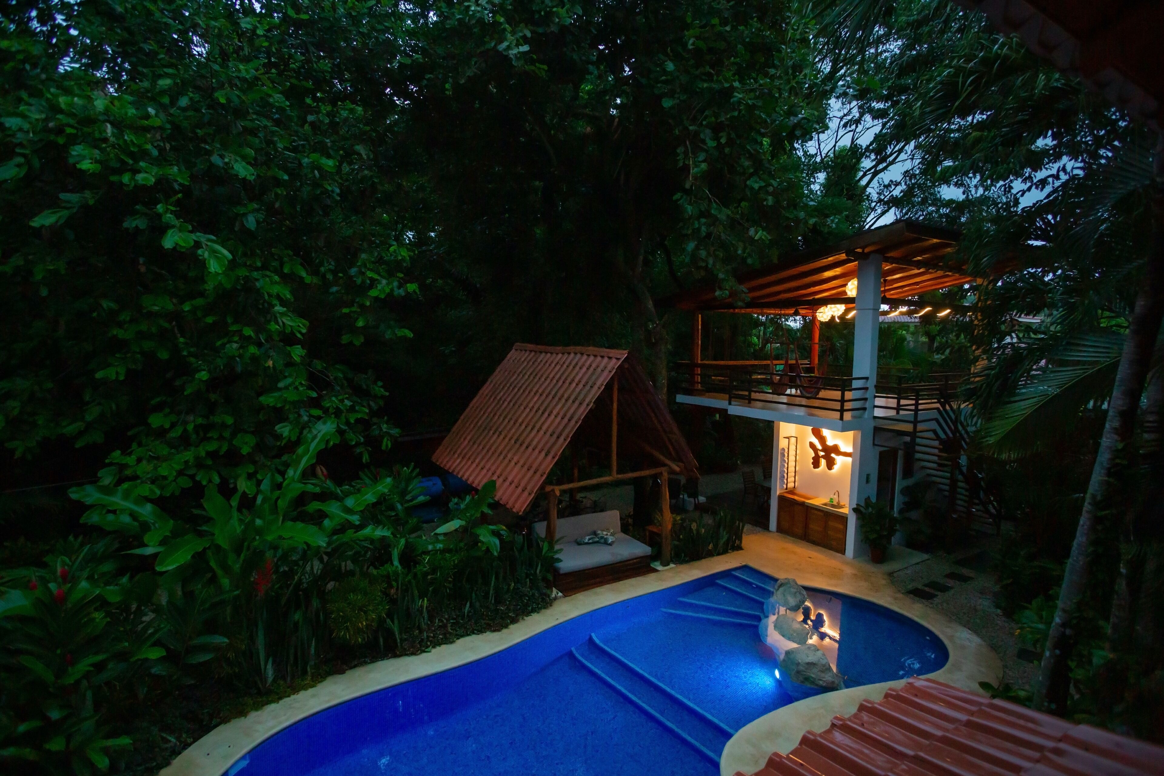A pool area with a wooden deck, a small wooden structure, and a covered seating area.