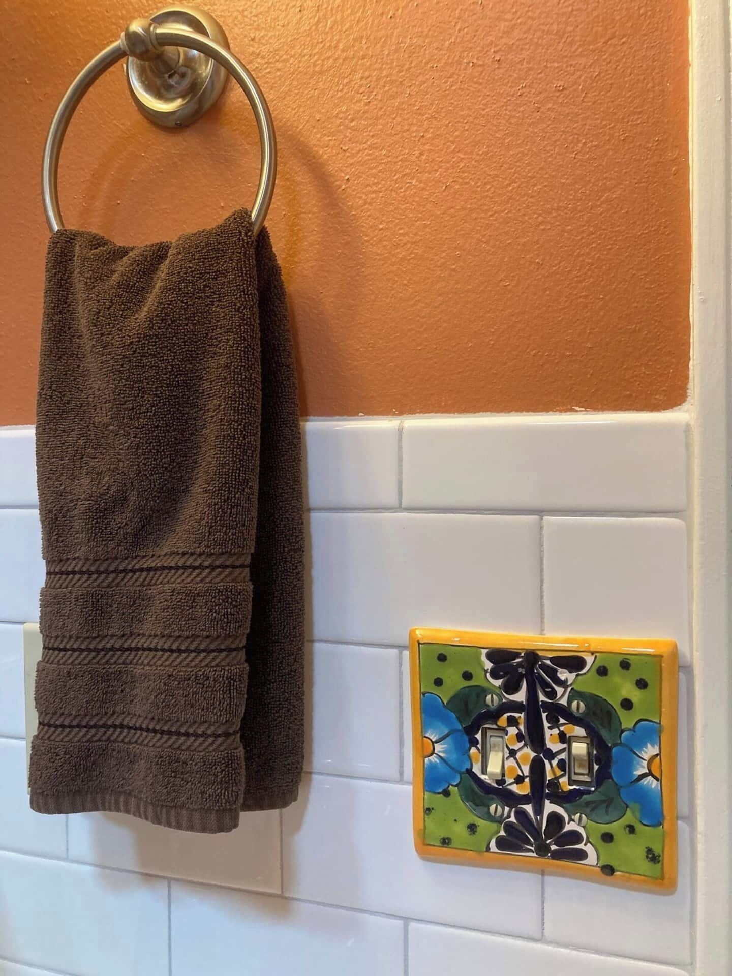 A bathroom with a towel hanging on a metal ring and a decorative tile with a floral pattern.