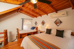 A room with a large bed, a smaller bed, a ceiling fan, an air conditioning unit, and wooden furniture.