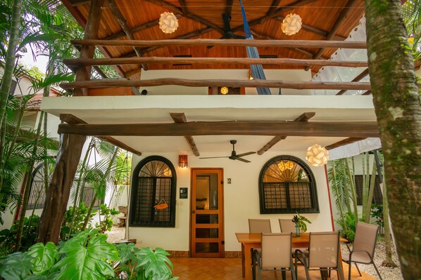 A two-story building with a wooden balcony, a dining area with a table and chairs, and a ceiling fan. - Villa Rio, Shady jungle pool, kitchen, 2 bedroom, amazing patios, walk to Samara beach (Sámara)