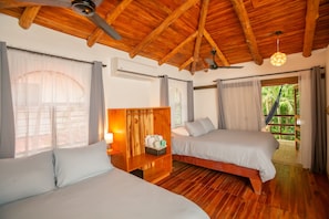 A room with two beds, wooden flooring, a ceiling fan, and a view of greenery outside. - Villa Rio, Shady jungle pool, kitchen, 2 bedroom, amazing patios, walk to Samara beach (Sámara)