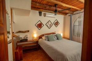 A bedroom with a wooden ceiling, a bed with white bedding, a nightstand with a lamp, and wall-mounted artwork.