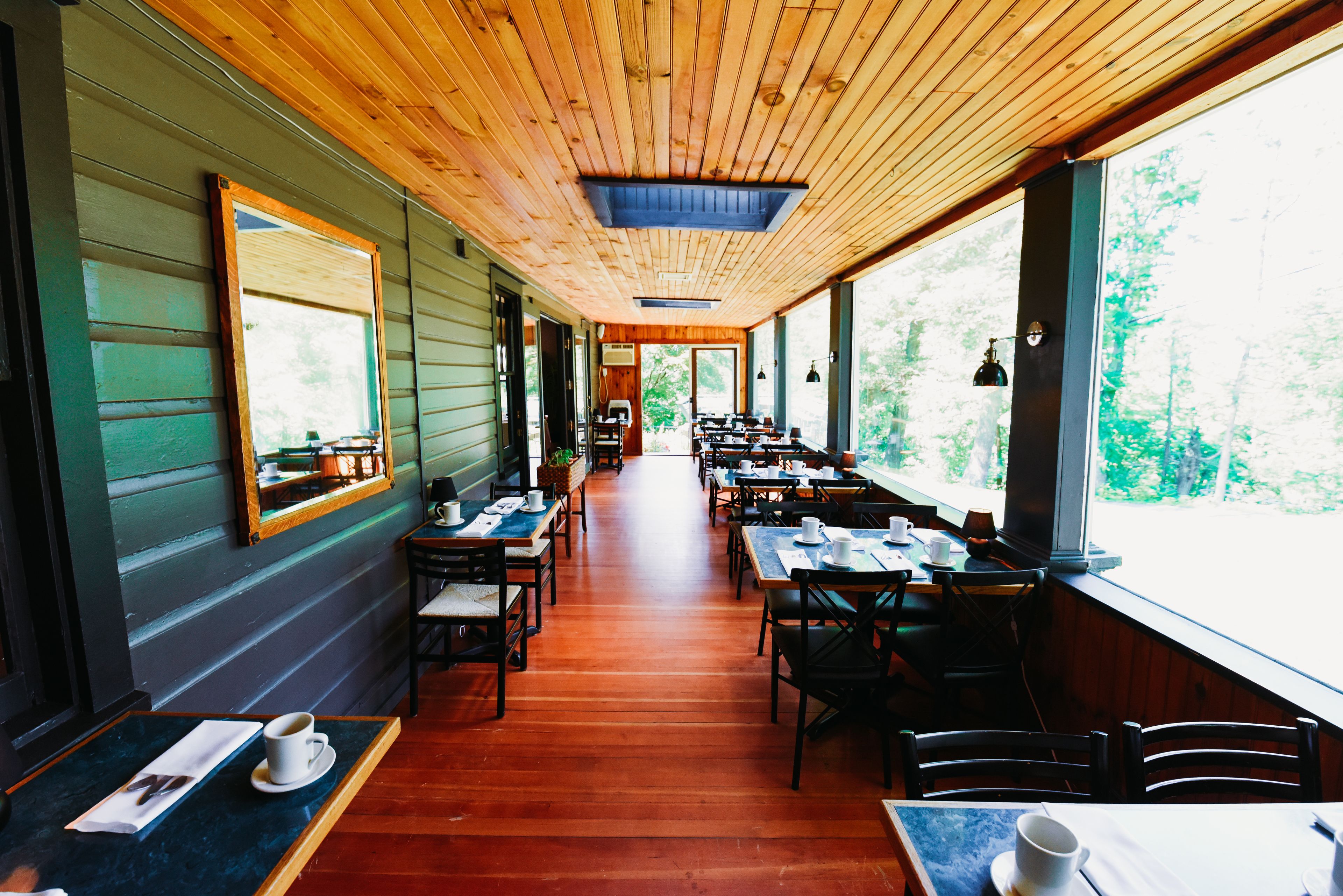 A long, narrow restaurant with wooden floors and walls, featuring tables and chairs arranged along the sides.