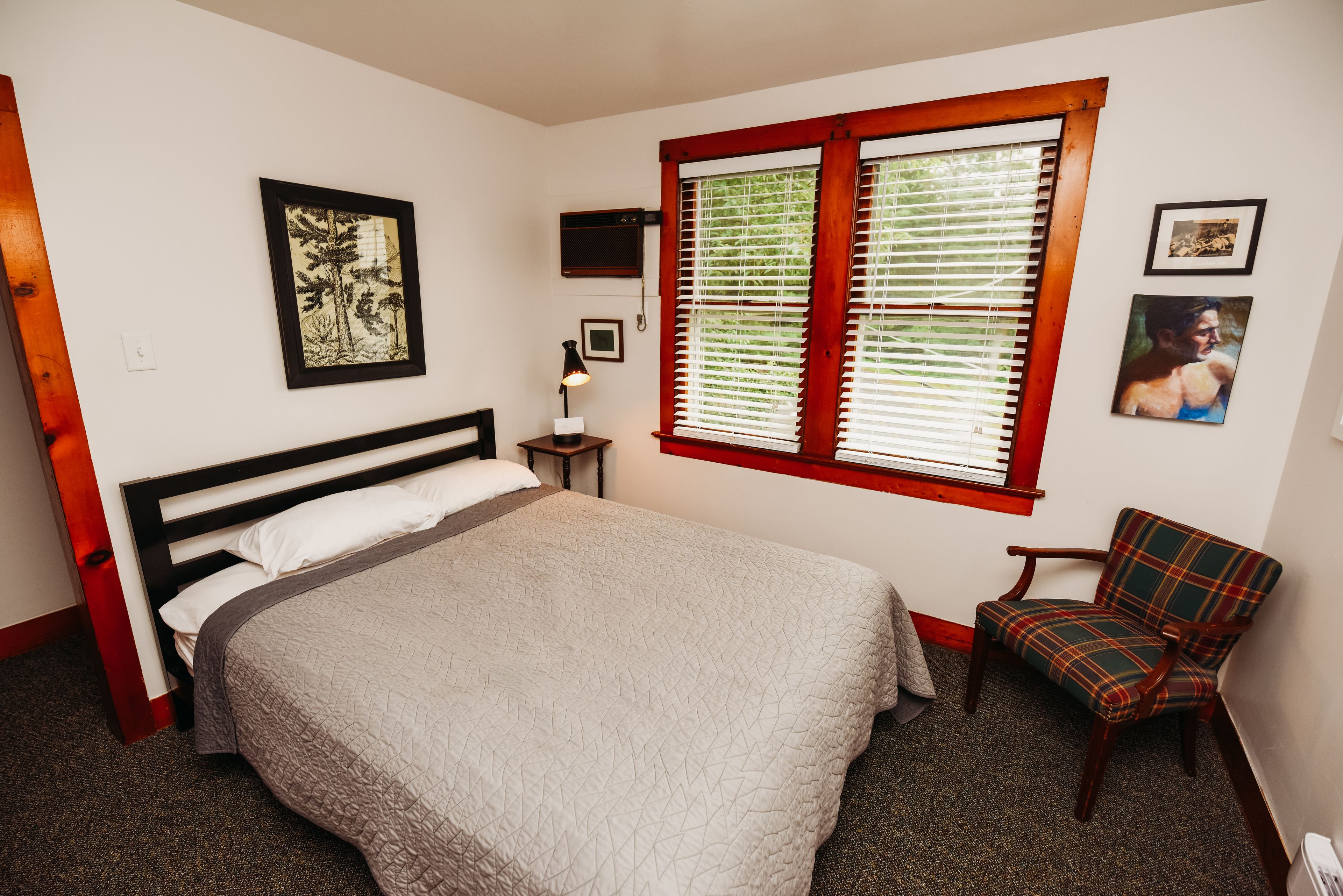 A bedroom with a bed, a chair, a window with blinds, a TV, and framed pictures on the wall.