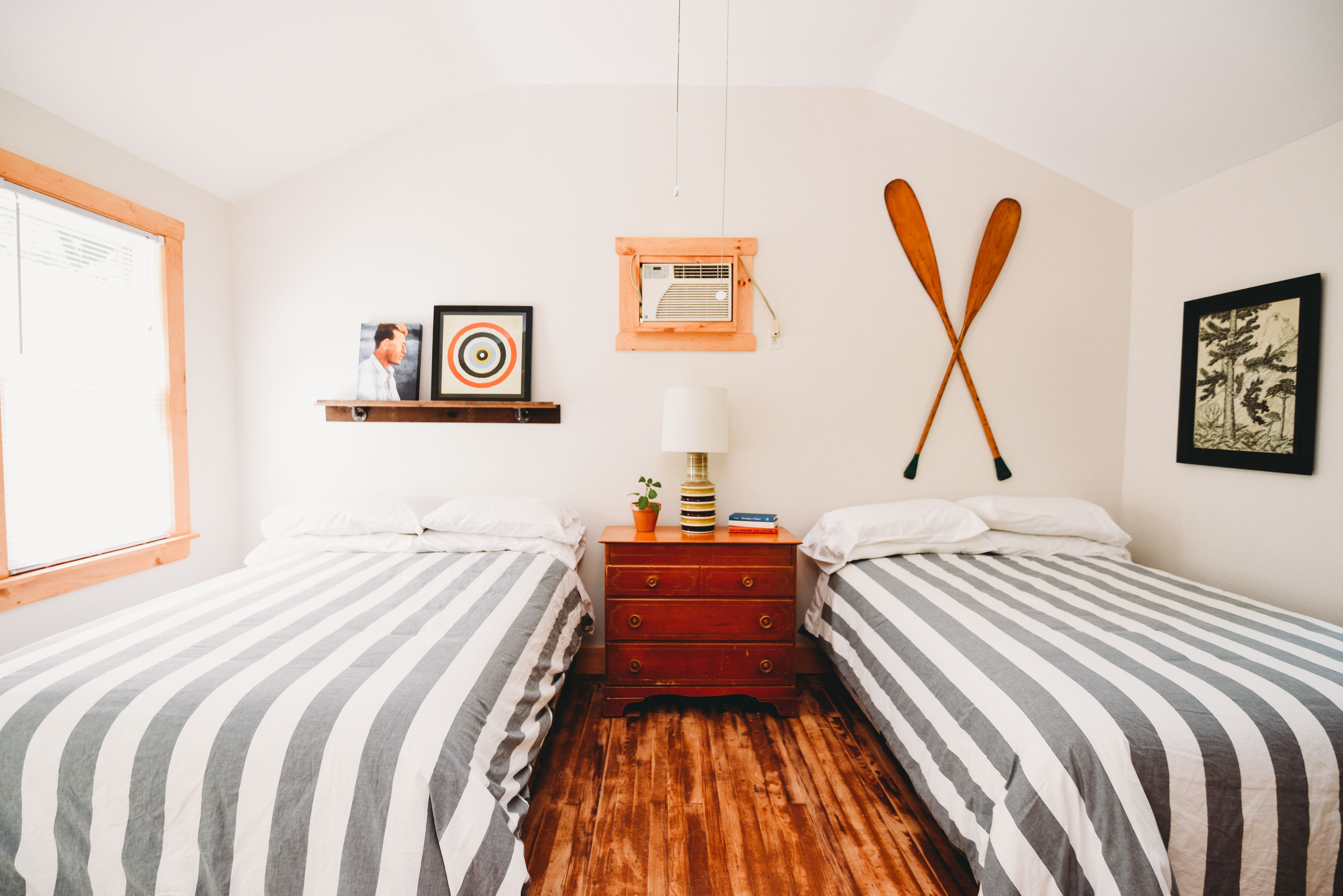 Un dormitorio con dos camas, un aparador, una ventana y aire acondicionado instalado en la pared.