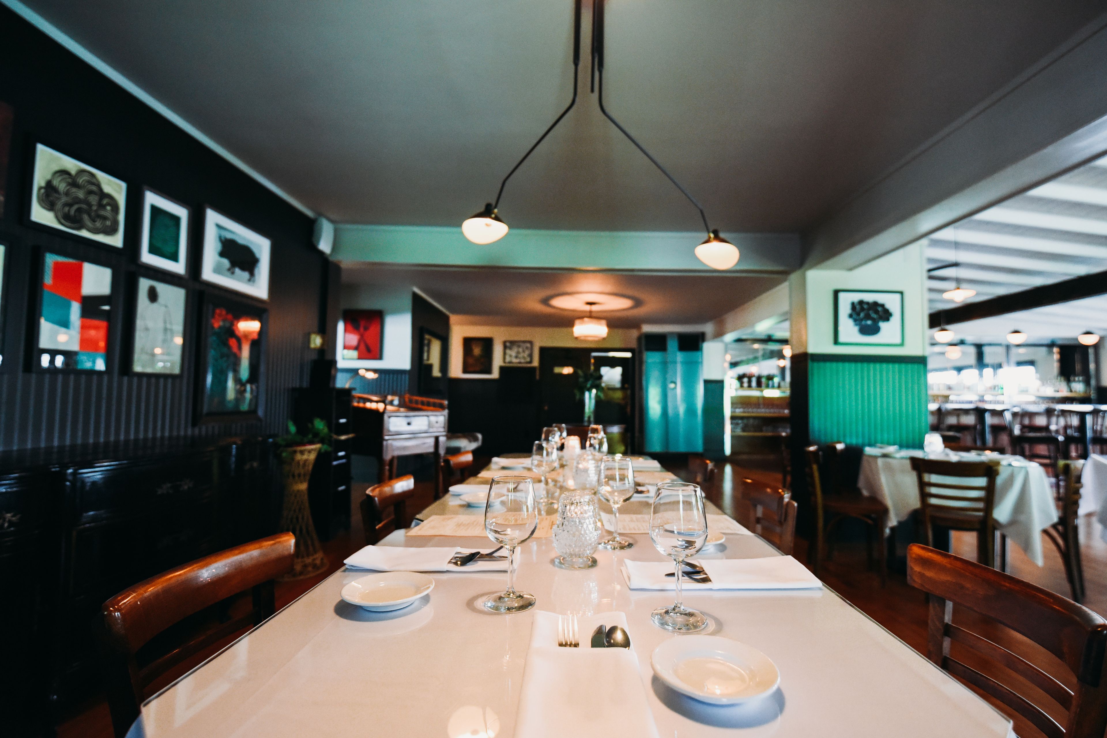 A restaurant with a long table set for a meal, featuring a variety of dishes and wine glasses.